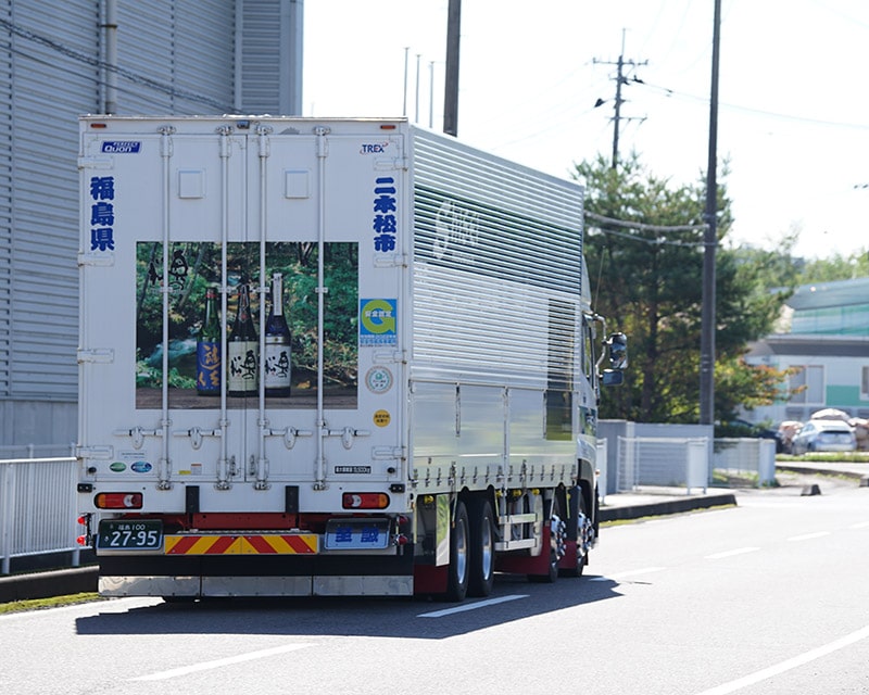 道路を走る二本松に因んだ絵柄の丸や運送トラック